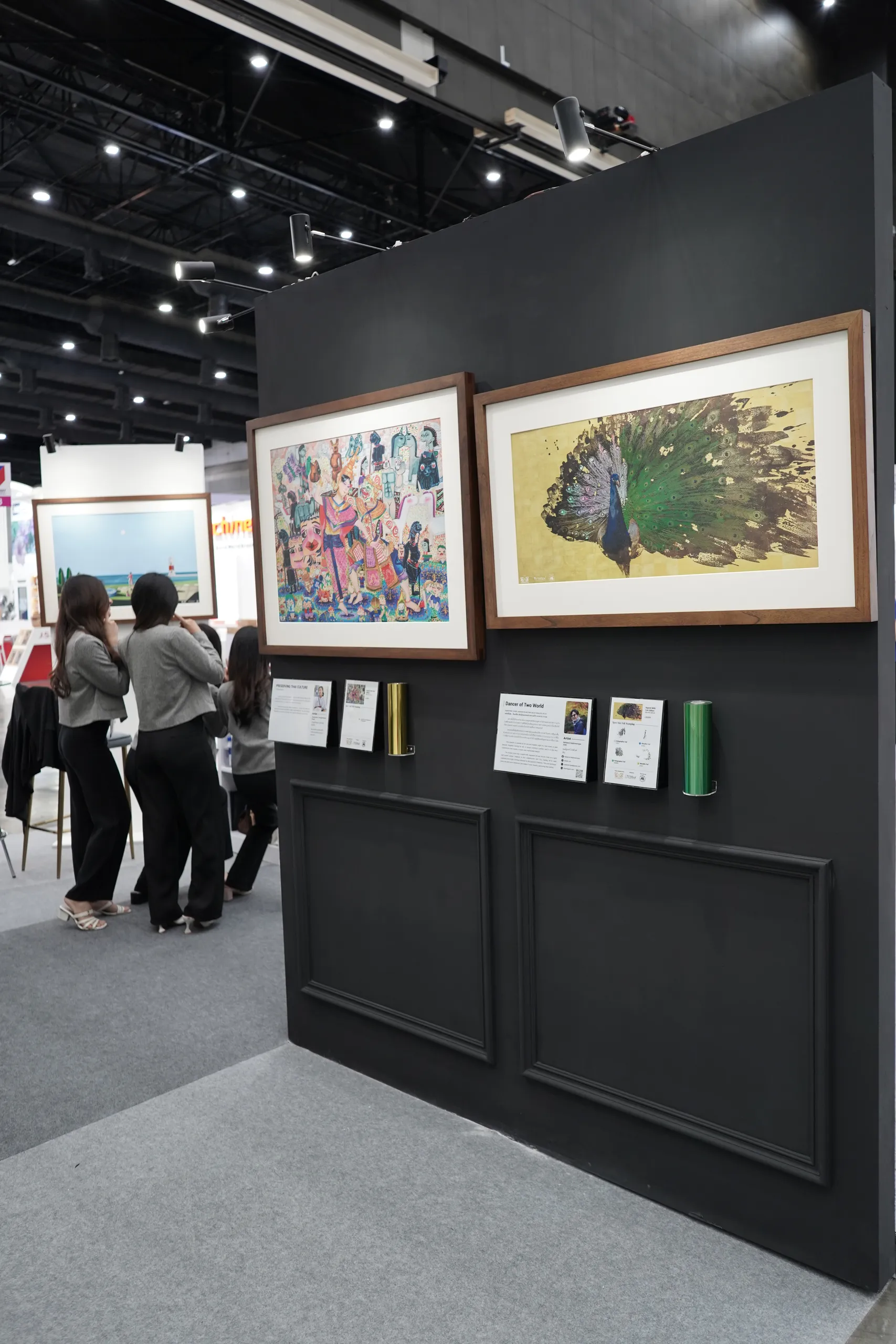 Visitors at the exhibition beside two framed works